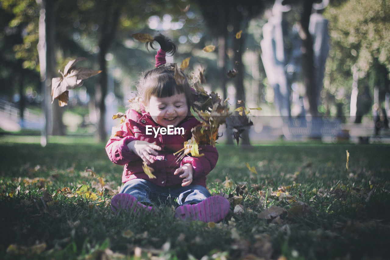 Full length of cute girl playing with autumn leaves while sitting on land