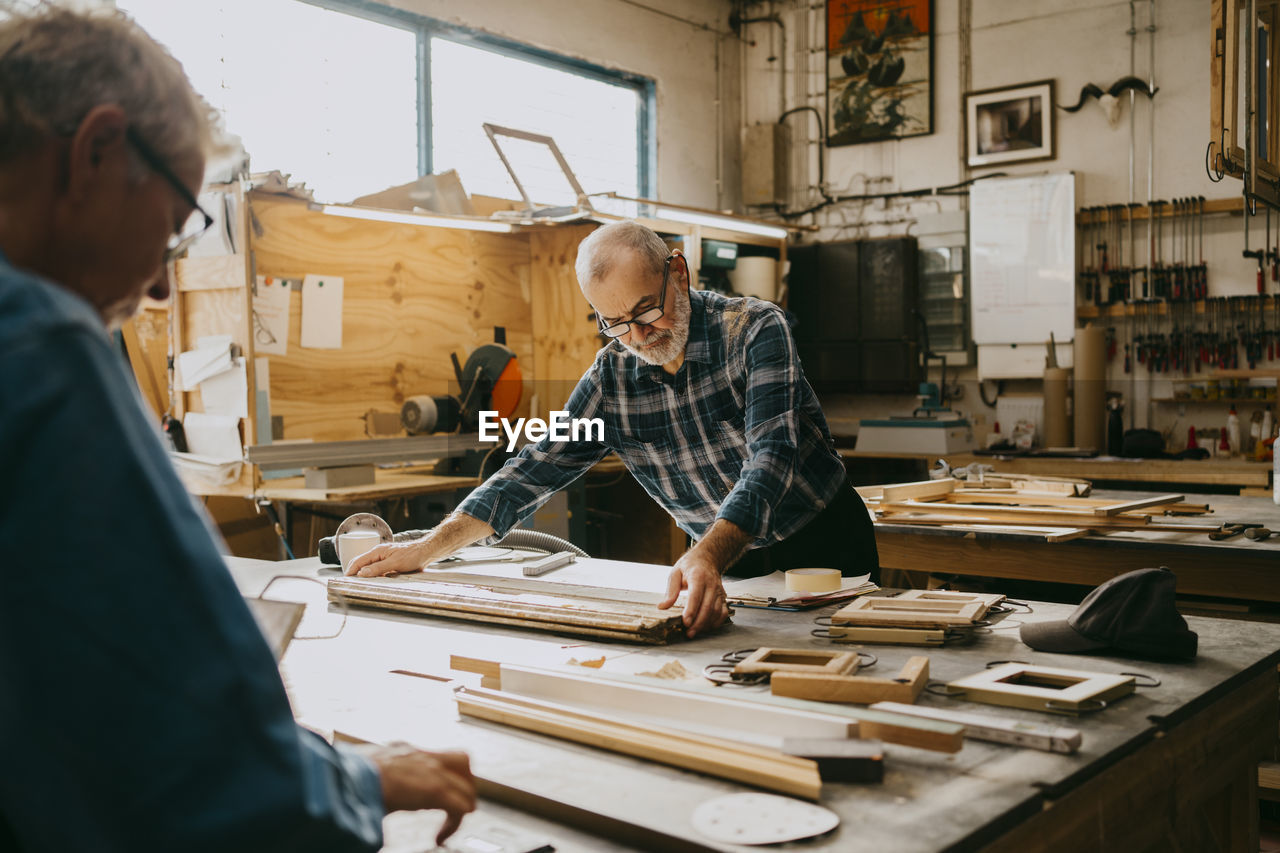 Senior male carpenter examining timber on workbench at repair shop