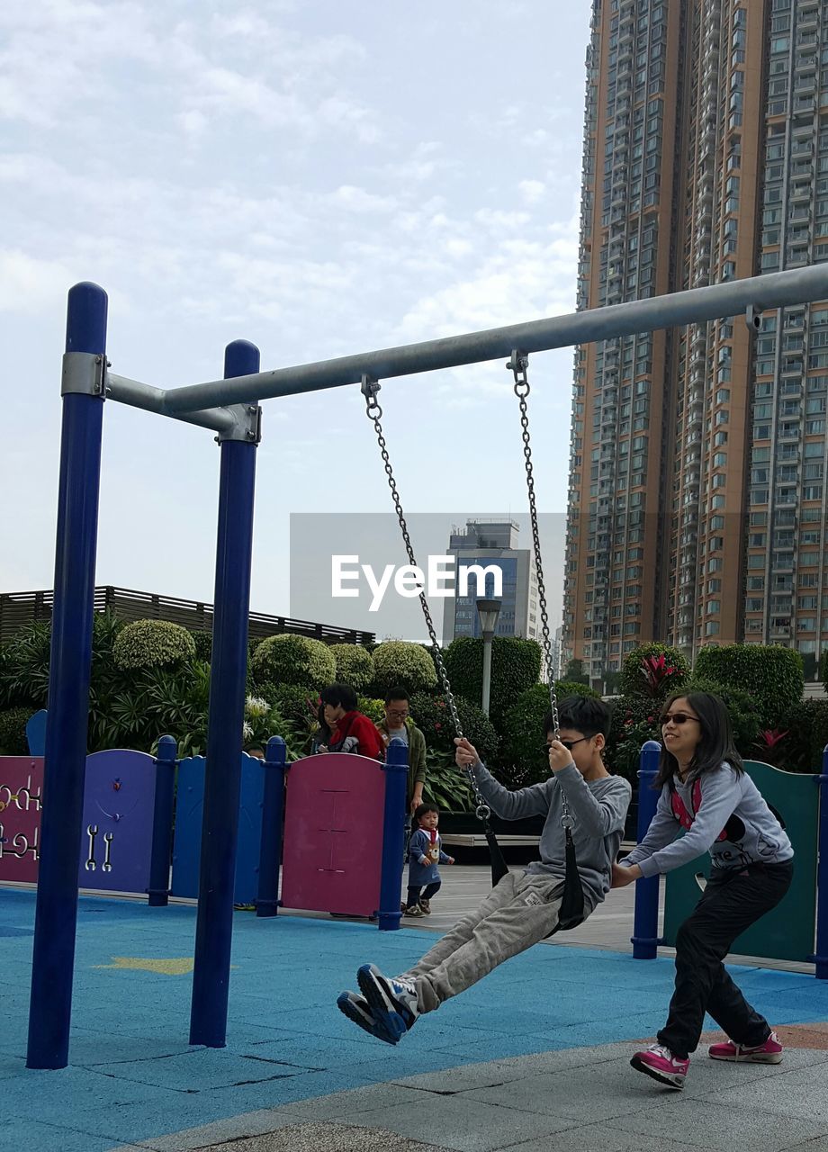 Sister pushing brother on swing at playground