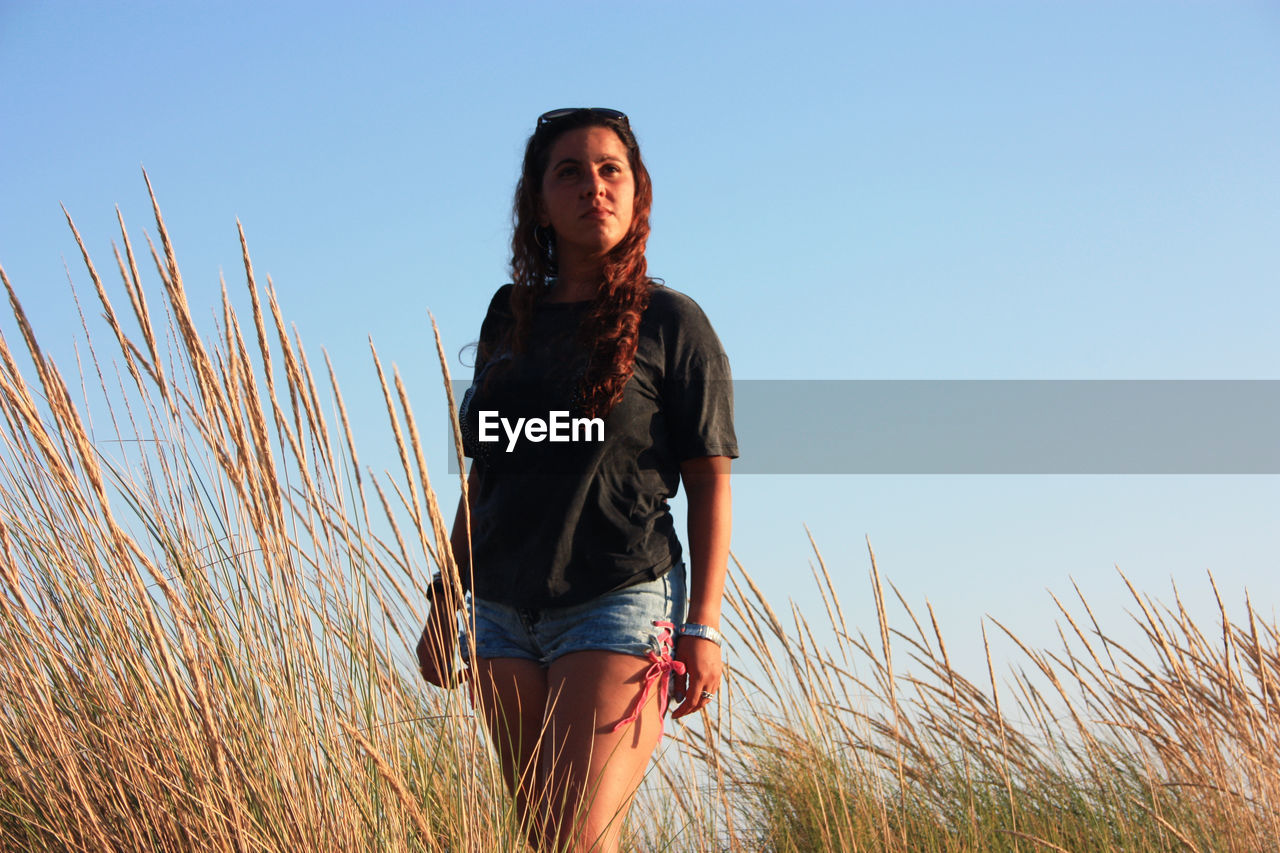 Young tanned woman in shorts at sunset time among the dry vegetation of sea sand dunes in tuscany