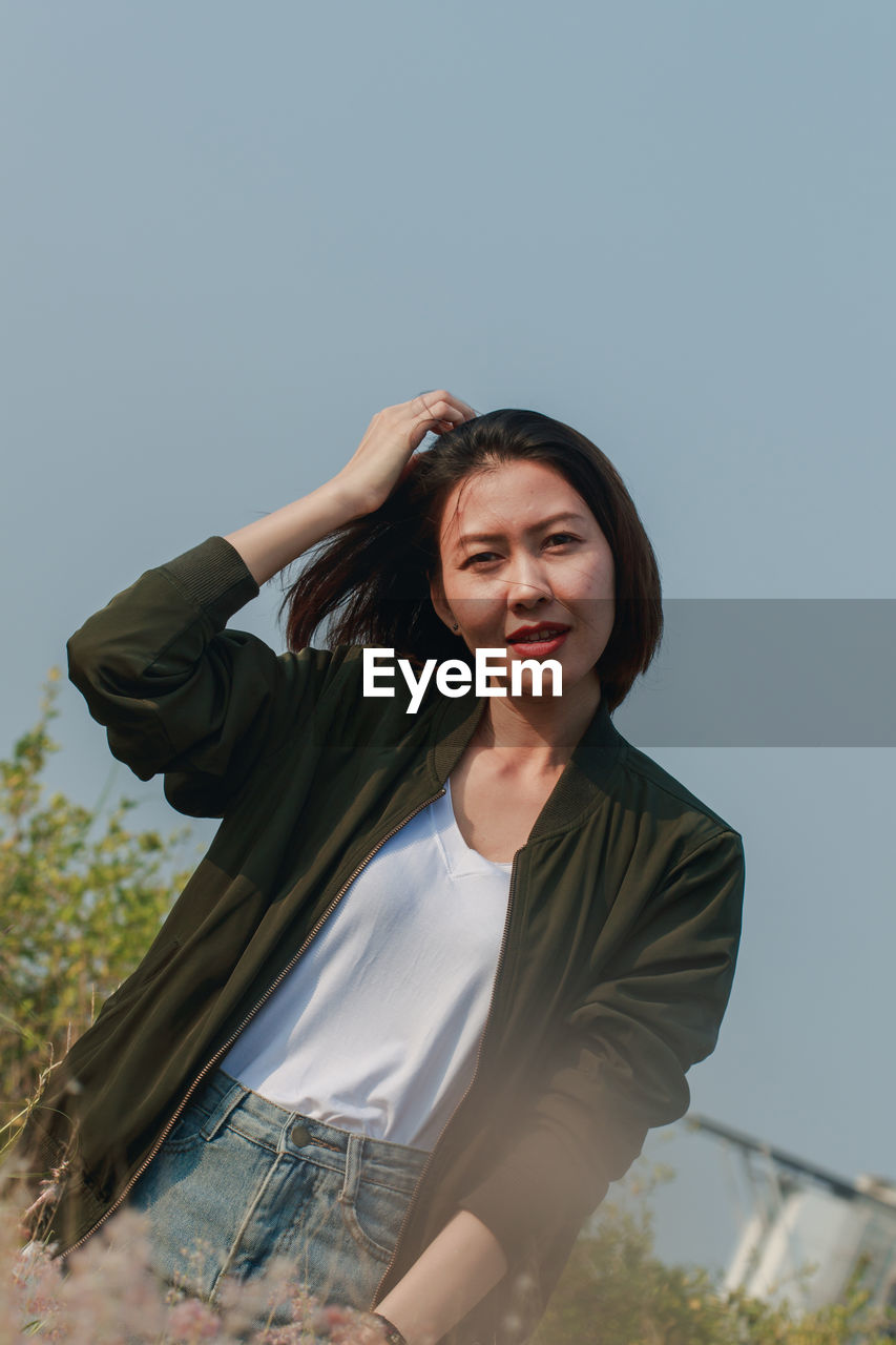 Portrait of beautiful young woman by plants against sky