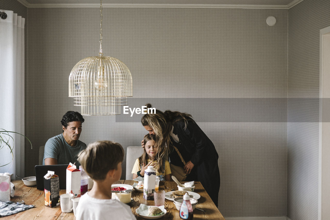 Mother kissing daughter over dining table at home