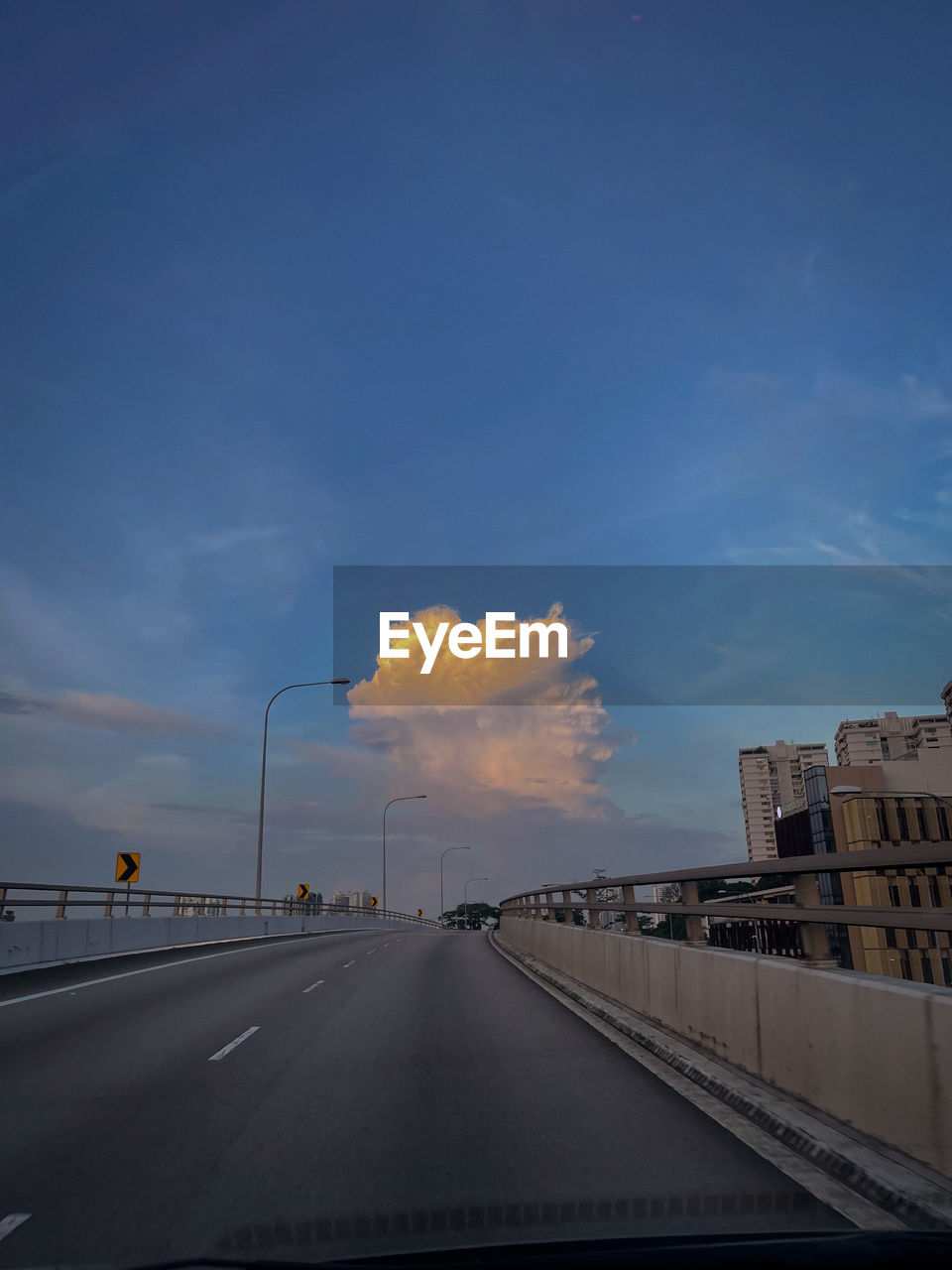 sky, transportation, cloud, road, horizon, dusk, architecture, city, car, nature, motor vehicle, sign, mode of transportation, sunlight, morning, street, built structure, the way forward, no people, travel, blue, highway, motion, light, outdoors, land vehicle, diminishing perspective, on the move, travel destinations, symbol, vanishing point, building exterior, marking, road marking