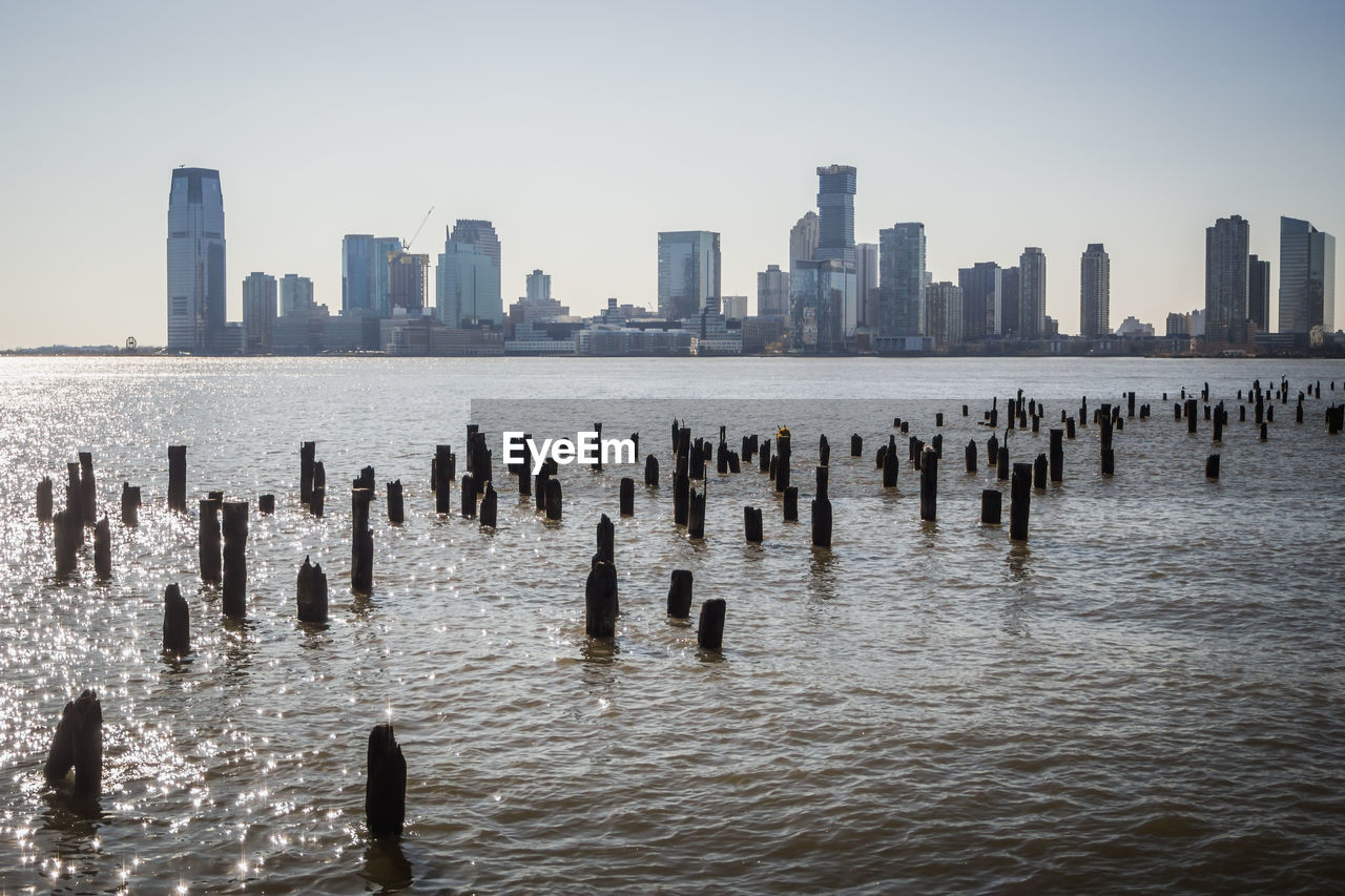 Wooden posts in sea against modern buildings in new york city