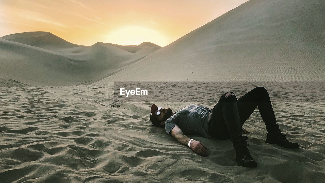 Man lying at desert during sunset