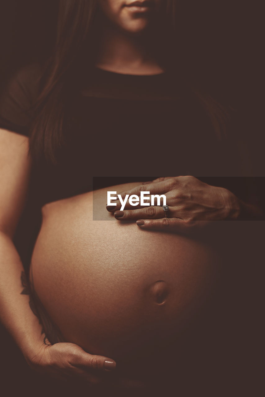 Midsection of pregnant woman over black background