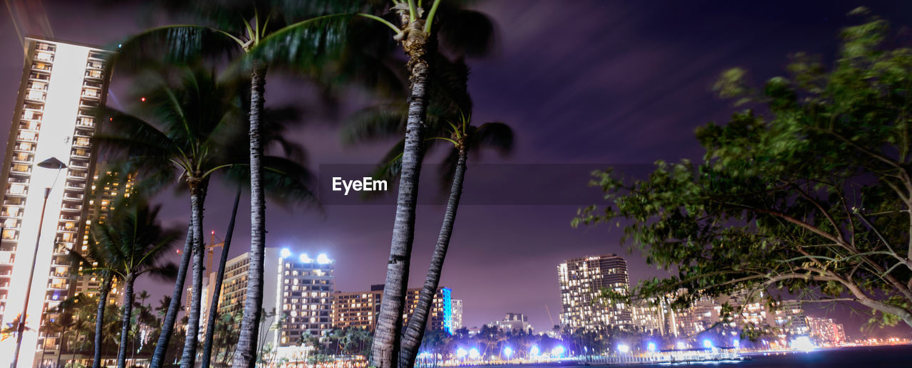 Panoramic view of trees and illuminated buildings against dramatic sky