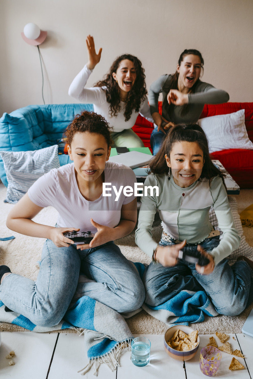 Cheerful multiracial female friends playing video game in living room at home