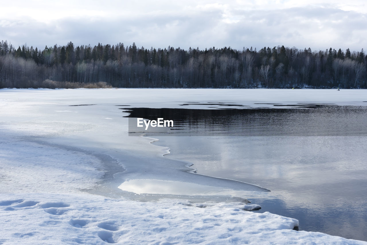 Melting of ice on the lake in early spring. trees, sky and clouds are reflected in the water.