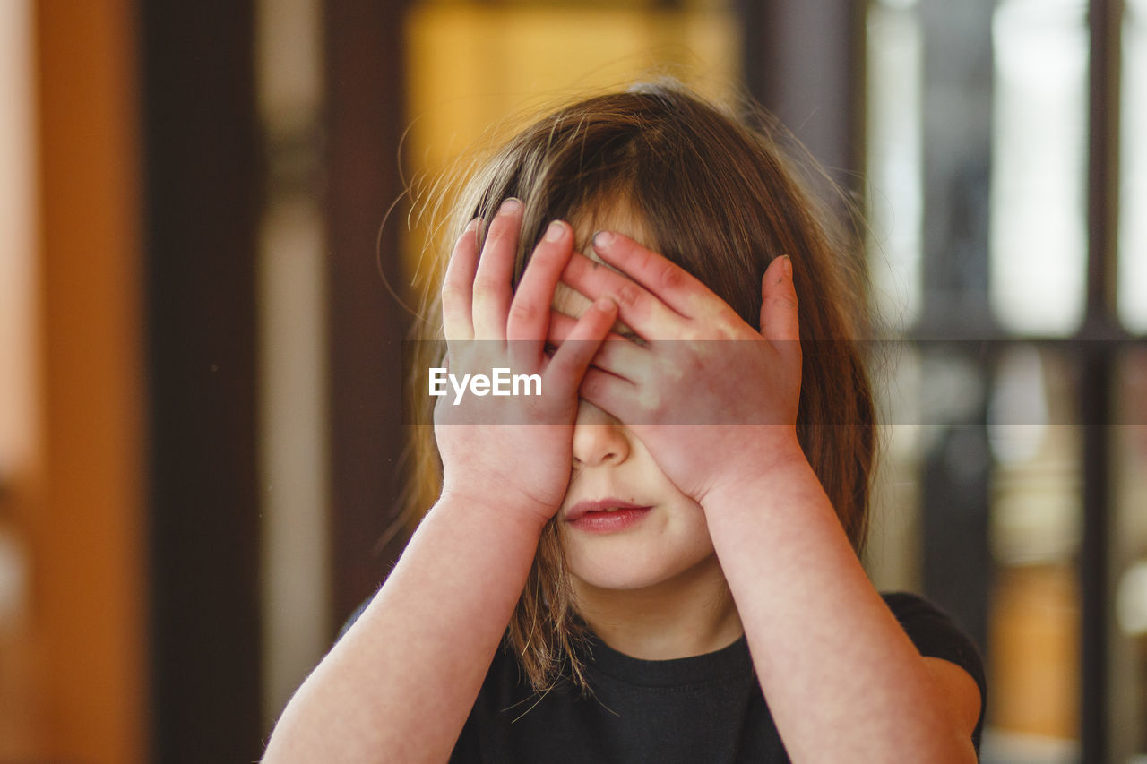 Close-up of a small child hiding behind her hands