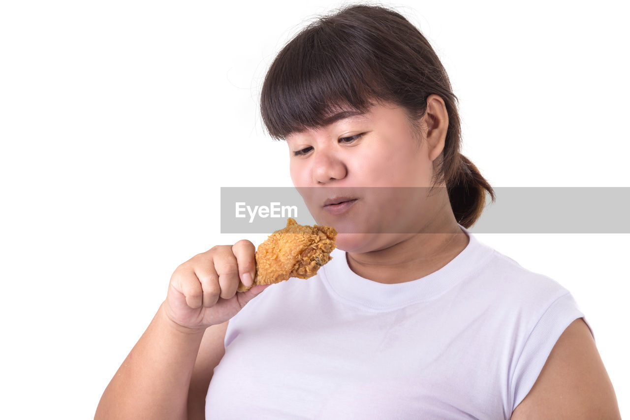 Young woman eating fried chicken meat against white background