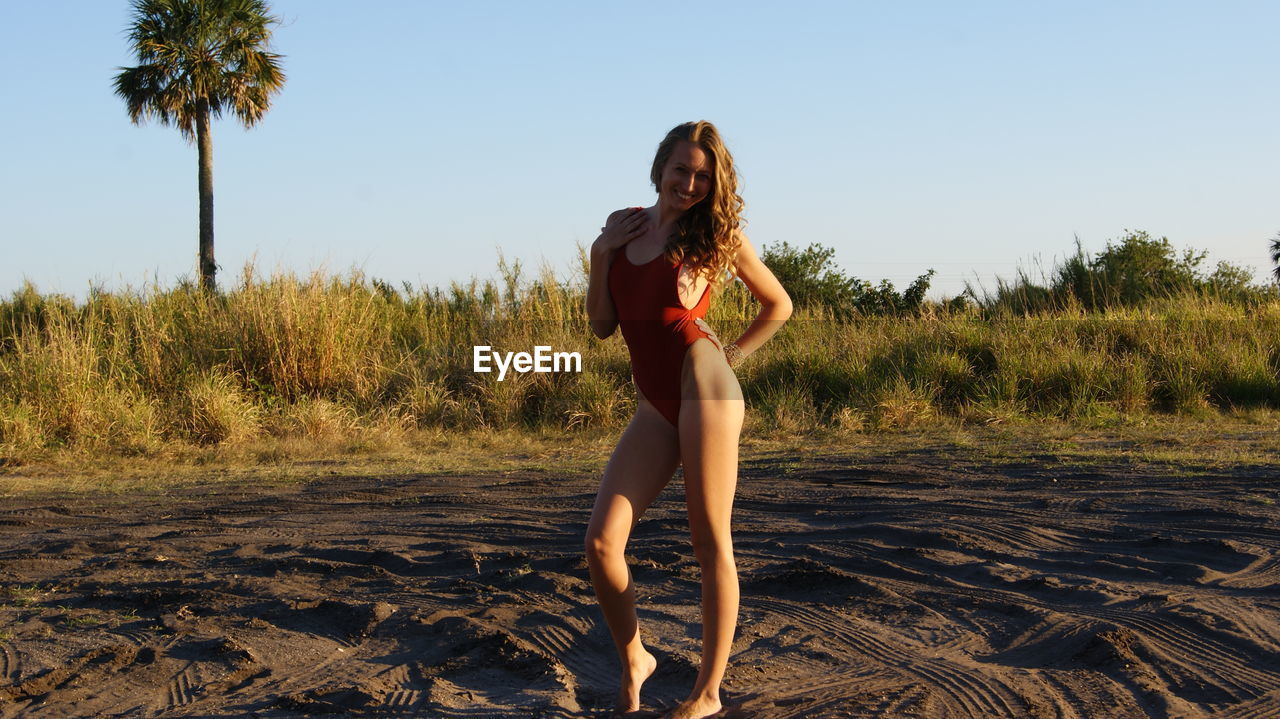 Full length portrait of sensuous young woman wearing one piece swimsuit on sand