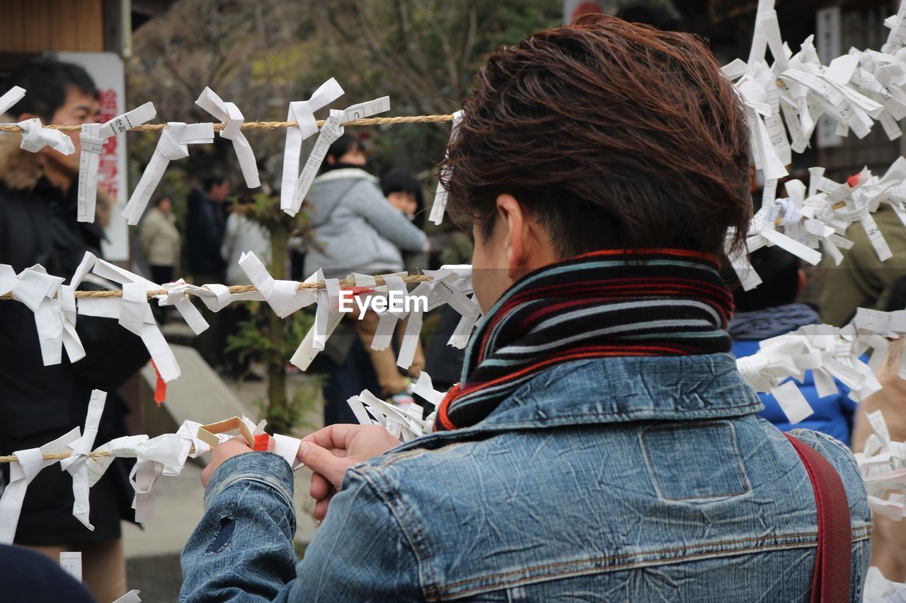 Rear view of boy tying paper on rope