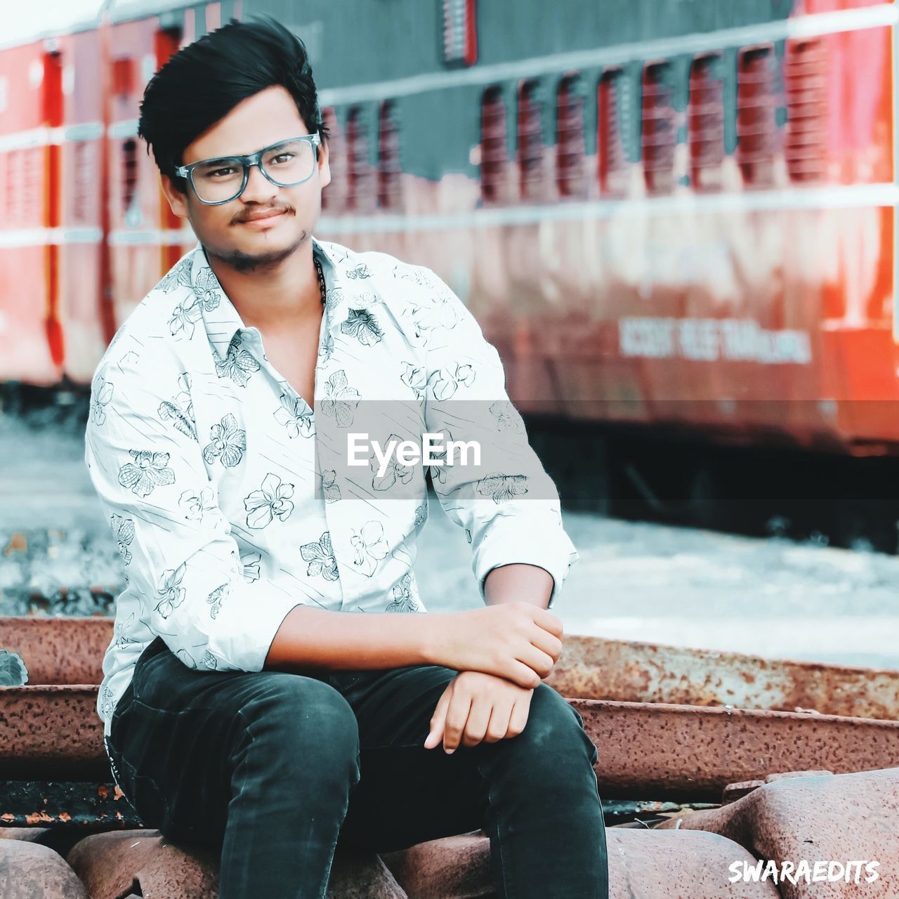 PORTRAIT OF YOUNG MAN SITTING AGAINST OUTDOORS