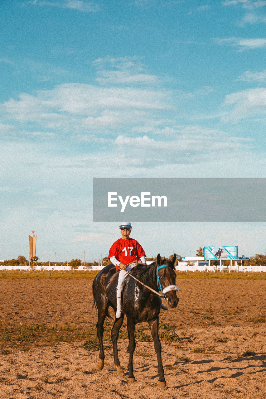 Rear view of young boy horse rider standing on field against clear sky