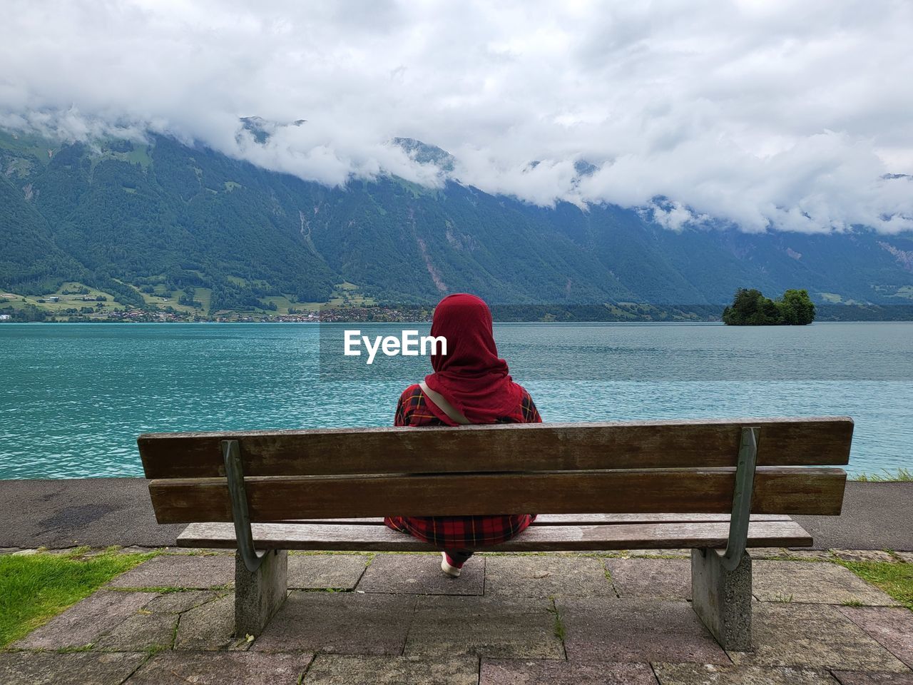 rear view of woman sitting on bench by lake against sky