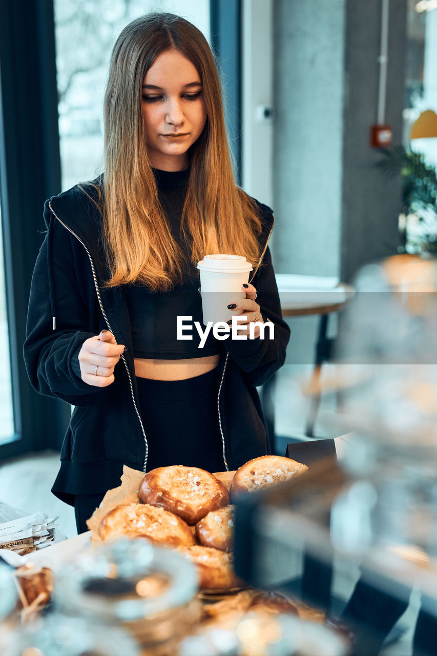 Woman holding cup with coffee looking at pastry, buns, cakes and cookies and waiting for the order