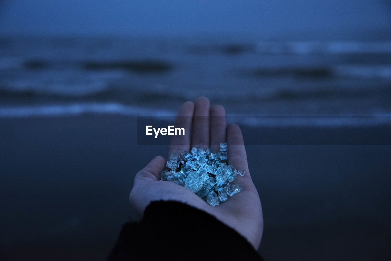 Cropped hand holding crystals at beach during dusk