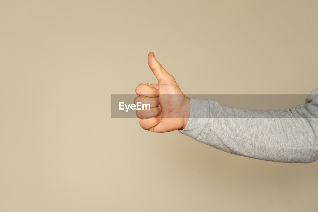 hand, studio shot, finger, arm, gesturing, indoors, one person, sign language, adult, copy space, hand sign, thumbs up, colored background, limb, communication, human limb, beige background, gray, close-up
