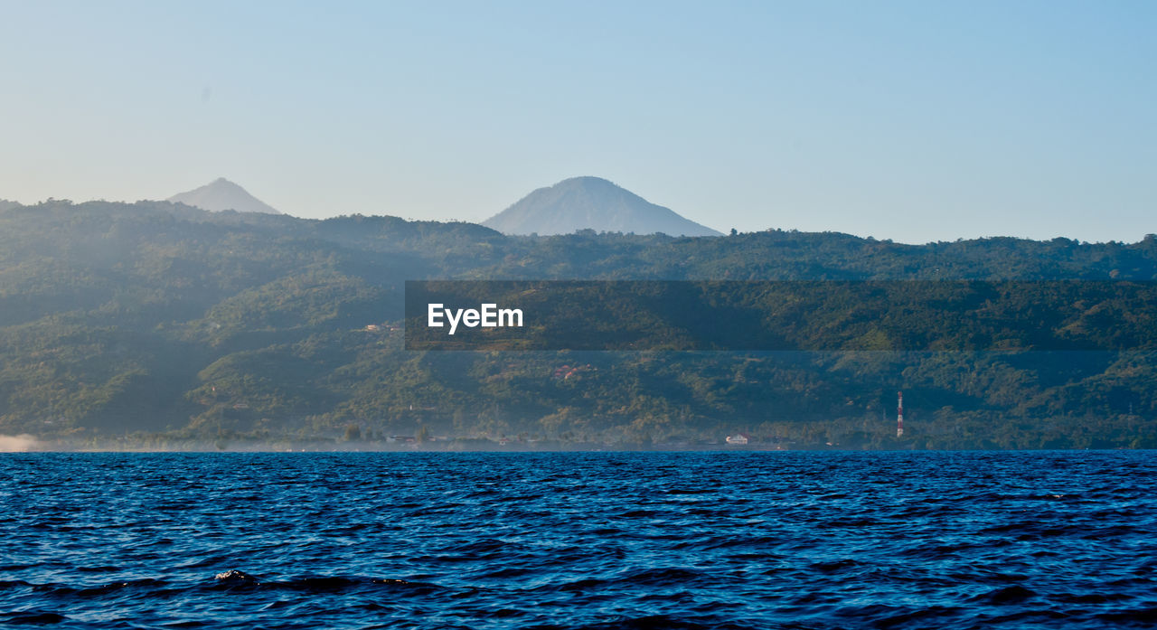 Scenic view of sea by mountain against clear sky