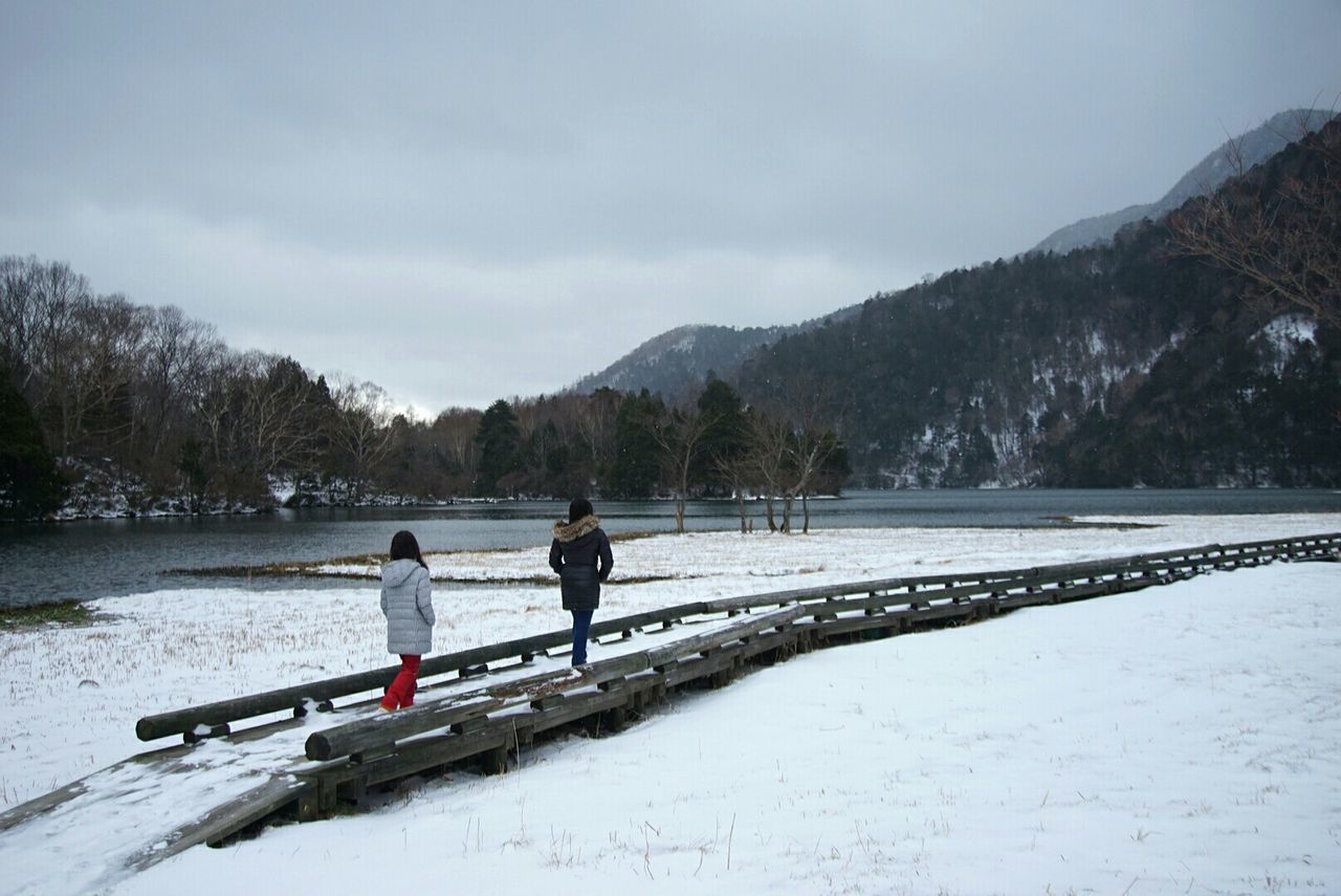 Woman walking on pathway amidst snow covered field against sky