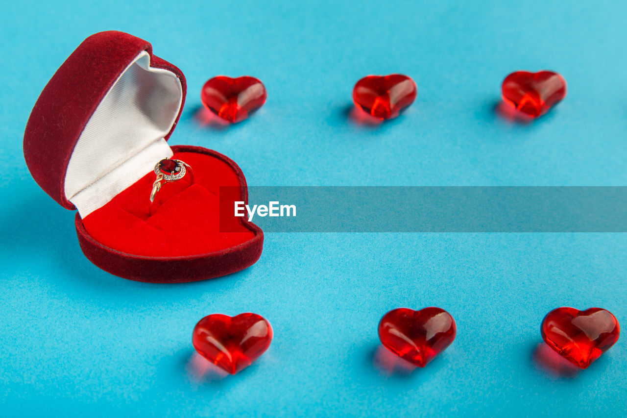 On a blue background, a box with a ring decorated with hearts and pebbles.