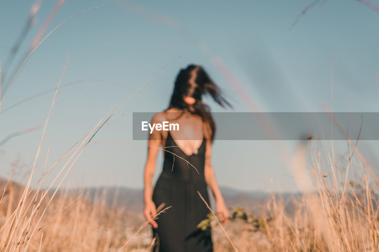 Woman standing on field against sky out of focus.