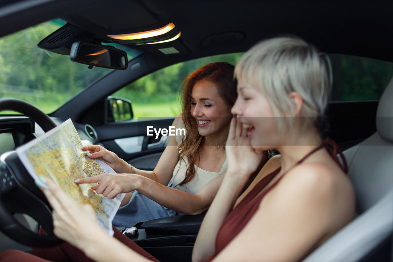 smiling friends using phone while sitting in car