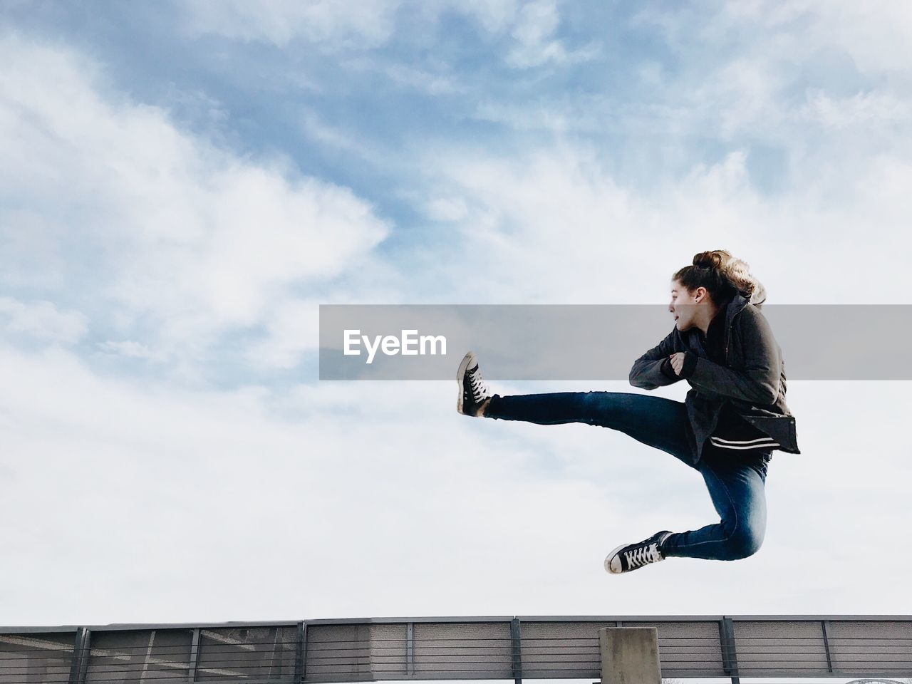 Full length of woman jumping against cloudy sky