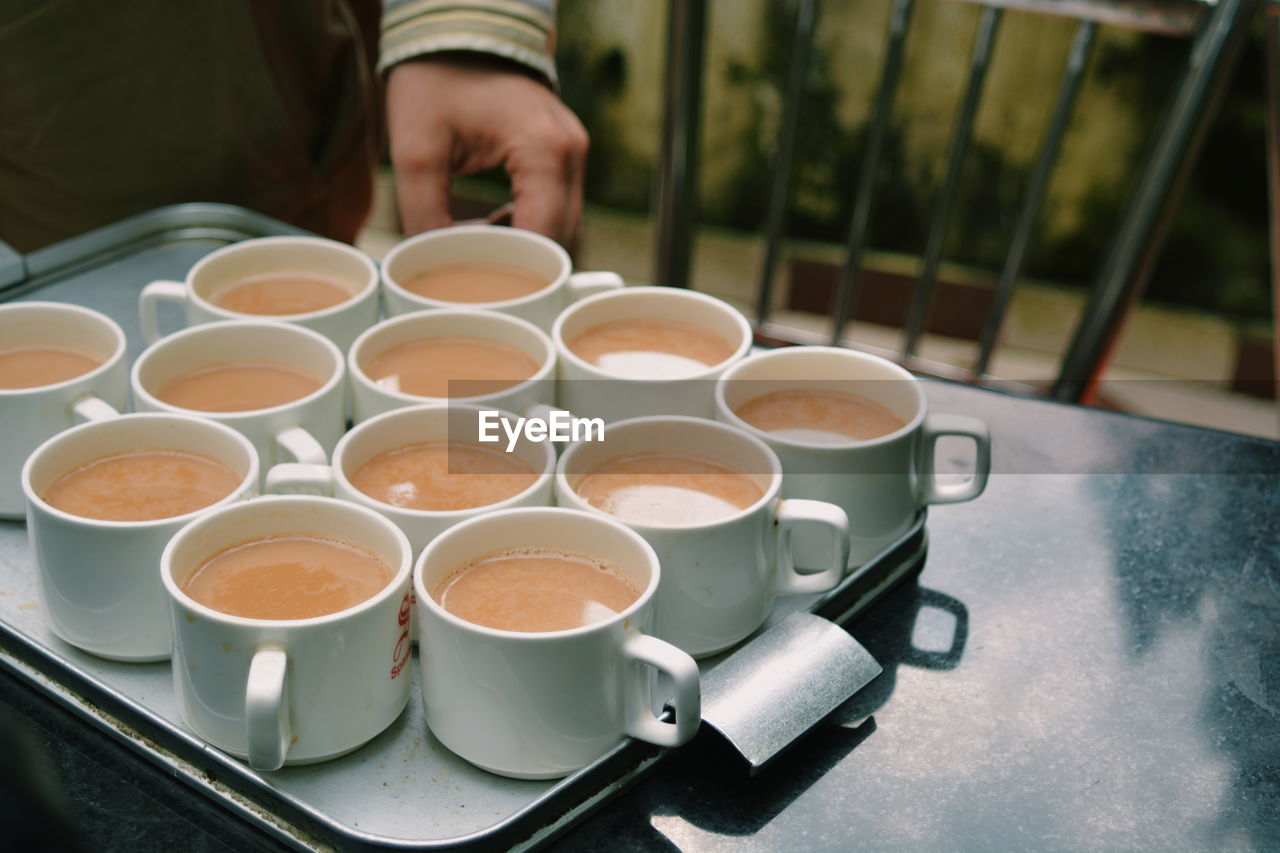 Midsection of man hand by tea cups in tray on table