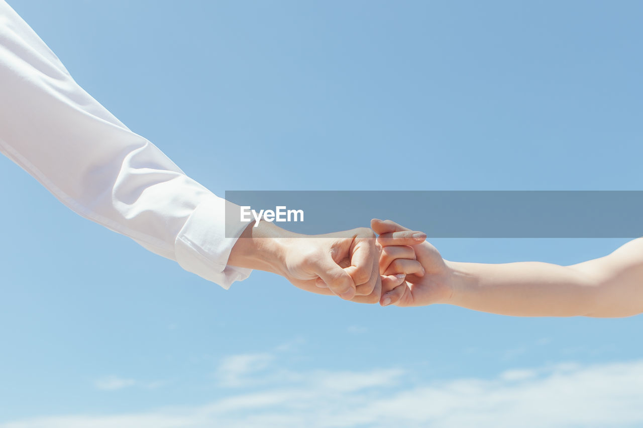 Cropped image of people holding little fingers against sky during sunny day