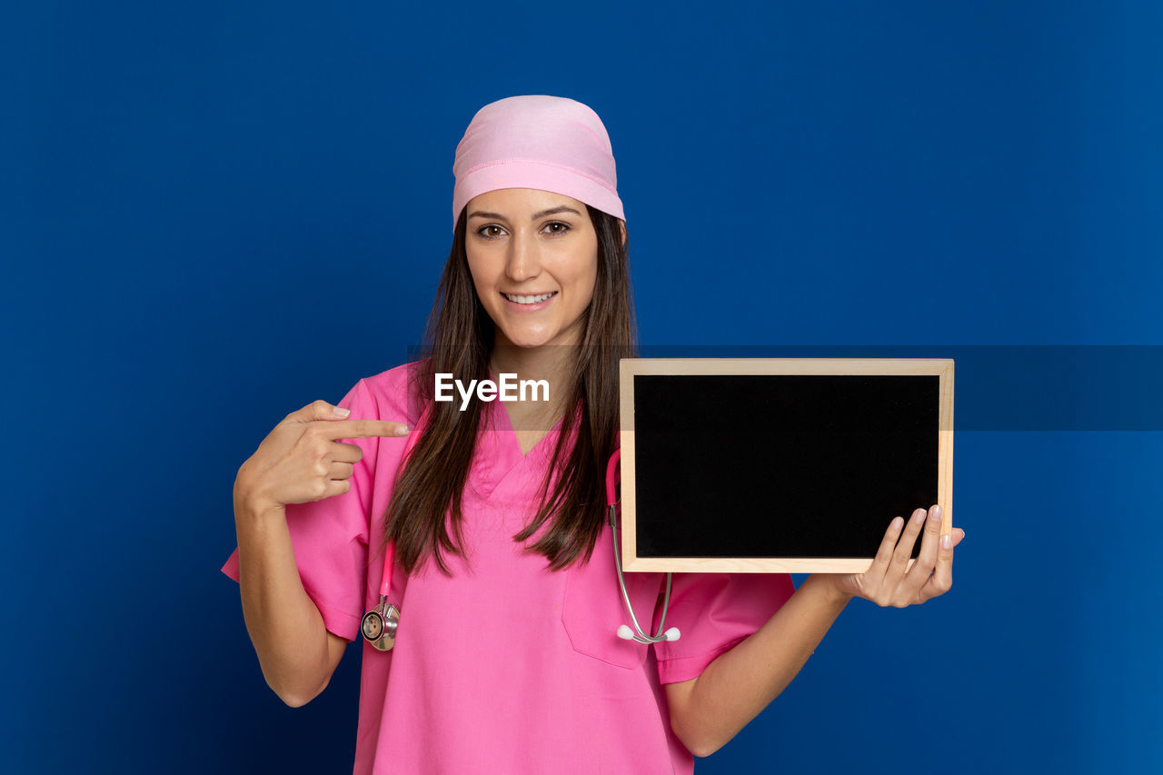 Portrait of smiling young woman standing against blue background