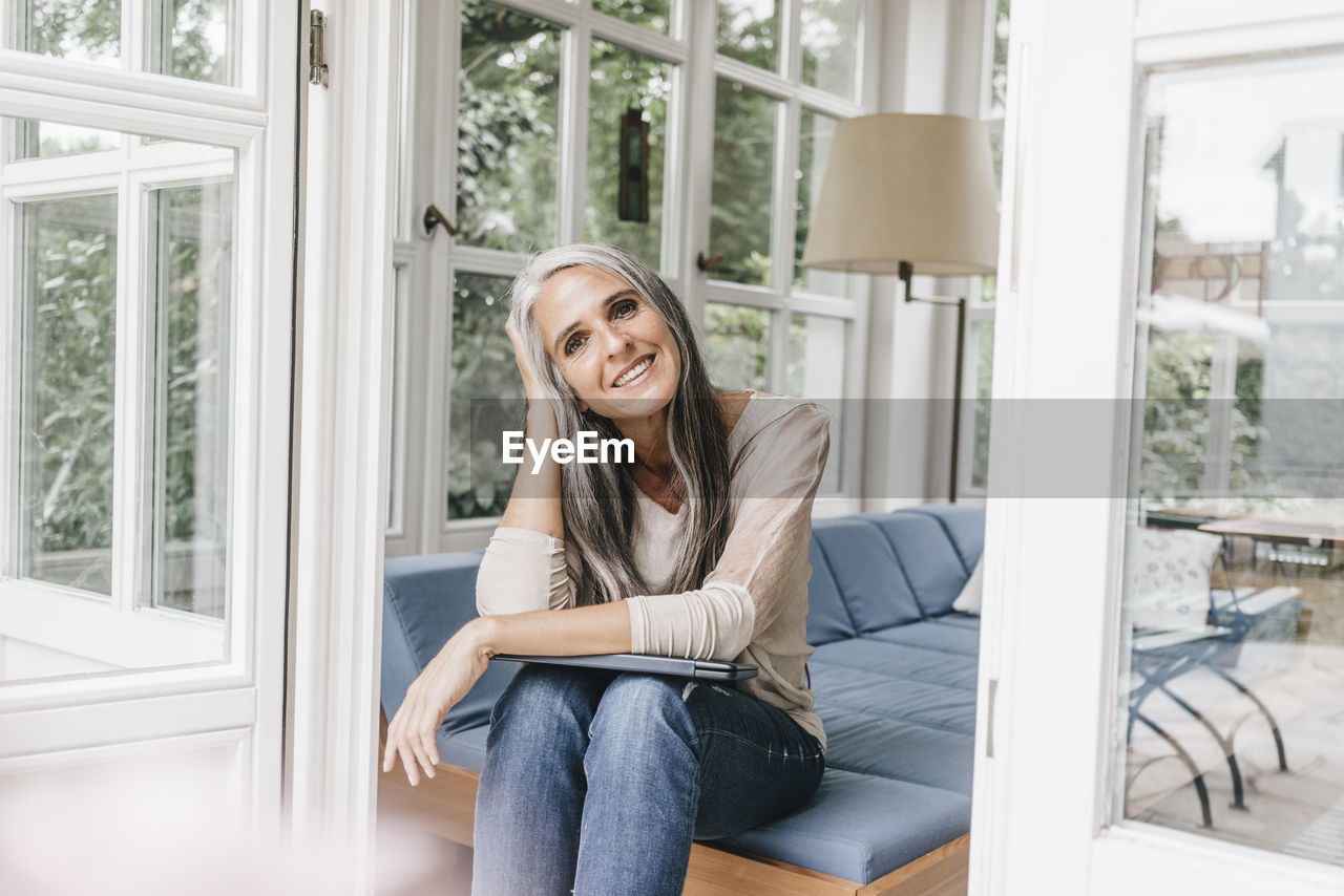 Smiling woman sitting on lounge in winter garden