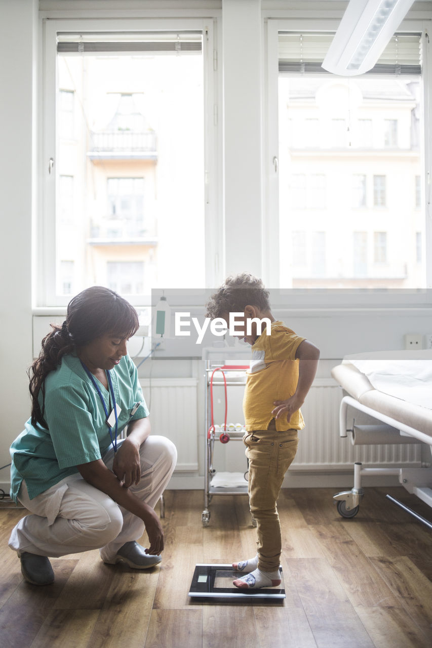 Mature doctor looking down while boy standing on weighing scale in clinic