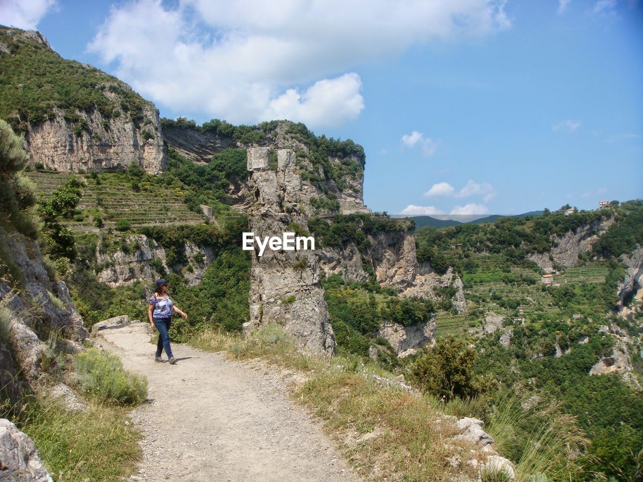 Full length of woman walking on dirt road at mountain against sky