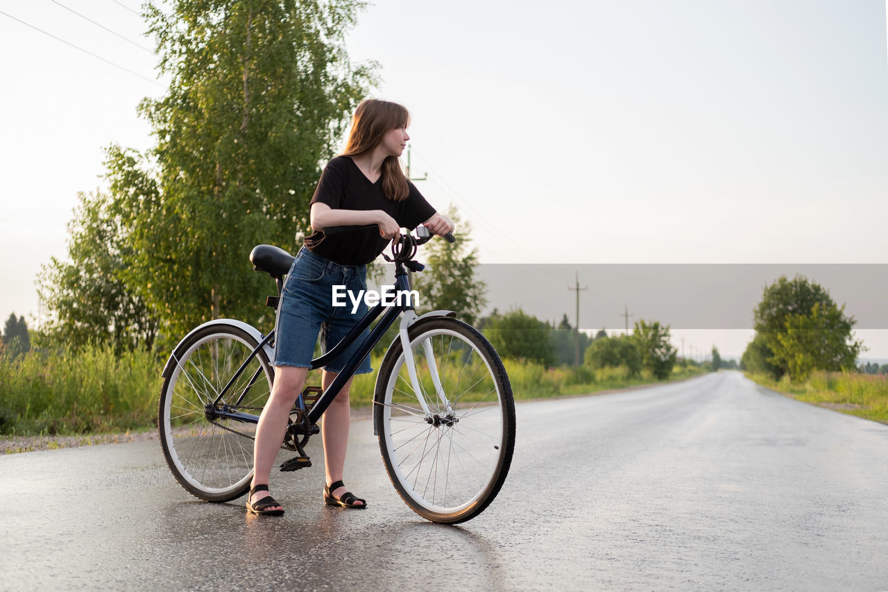 Woman with bicycle standing on road