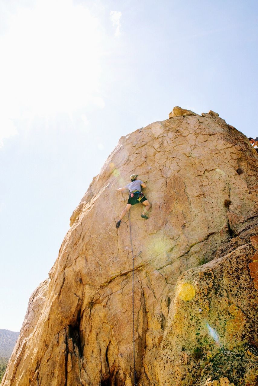 Low angle view of man climbing rock against sky on sunny day