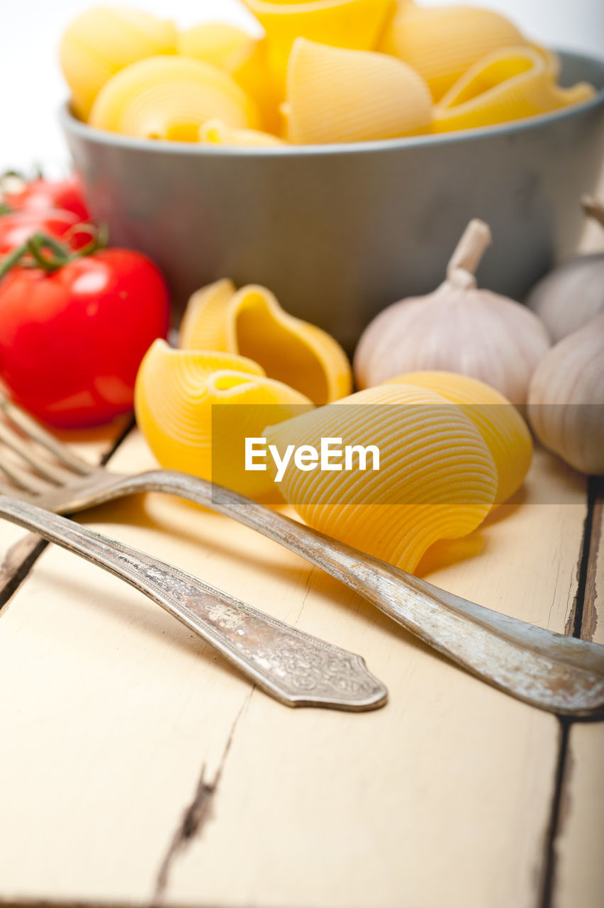 Close-up of raw pasta with tomato and garlic on wooden table