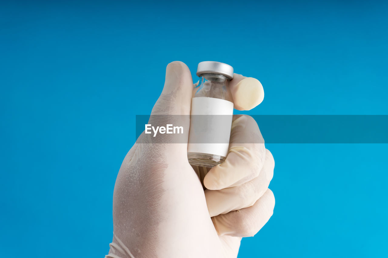 Cropped hand of person holding vial against blue background