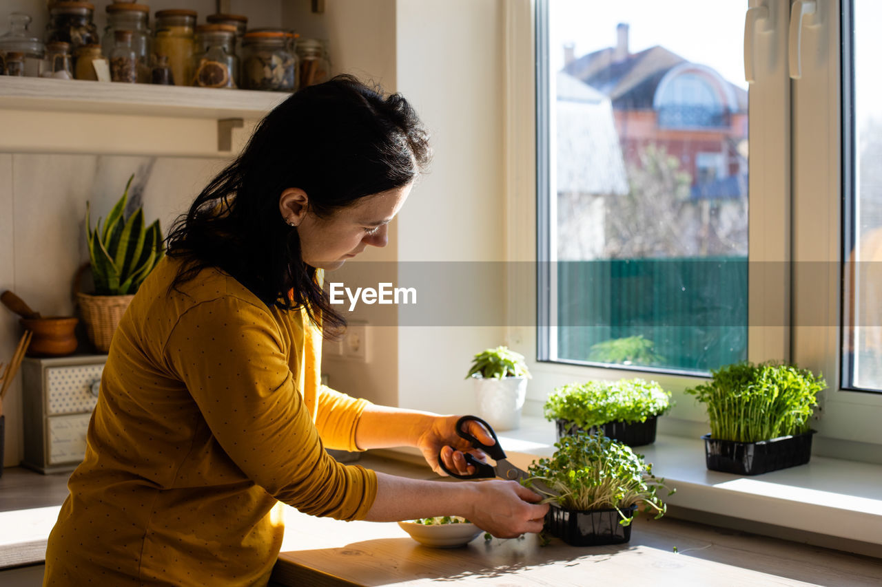 Side view of woman looking at potted plant at home