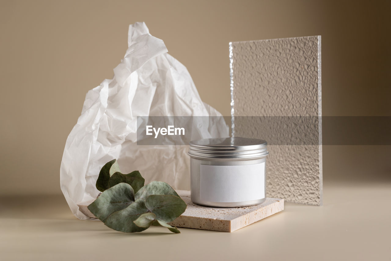 Face cream composition in a metal jar on a beige background with stone, glass and eucalyptus leaf
