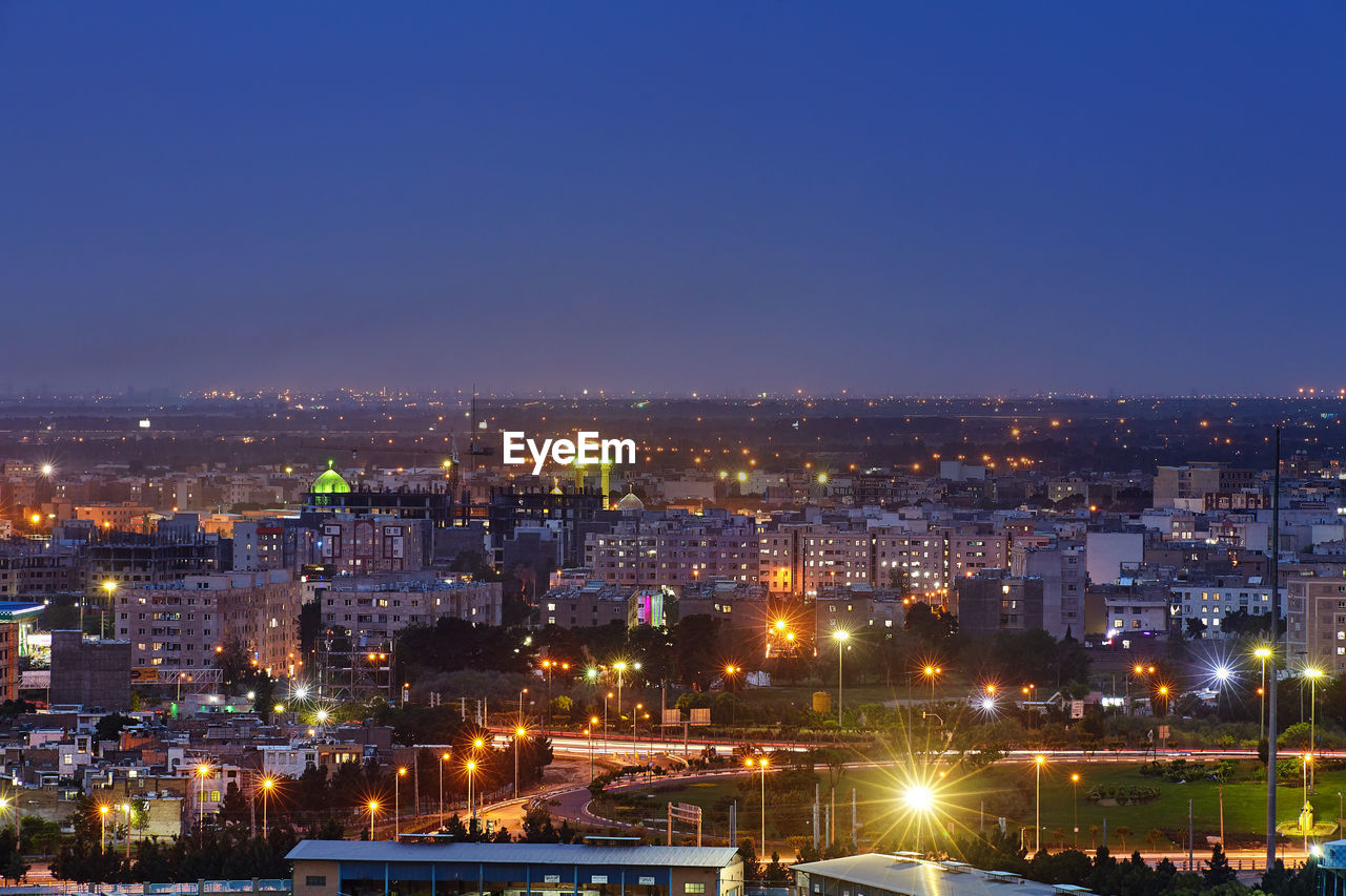 HIGH ANGLE VIEW OF ILLUMINATED BUILDINGS AGAINST CLEAR BLUE SKY