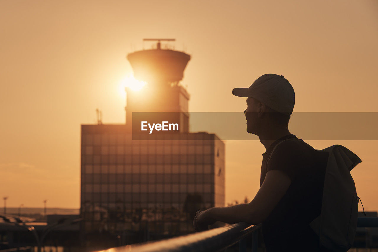 Traveler with backpack at airport. silhouette of man against air traffic control tower at sunset.
