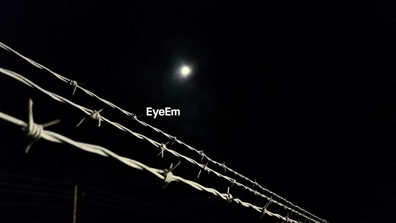 Low angle view of barbed wire against clear sky at night