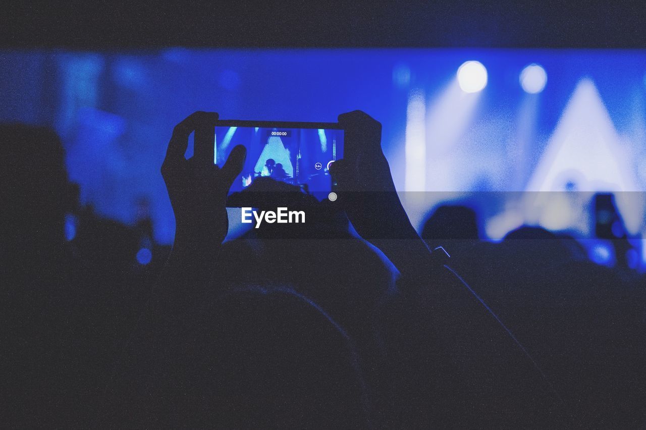 Cropped hands of person photographing with mobile phone in music concert at night