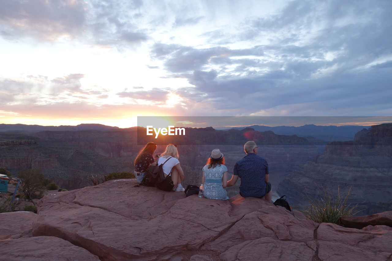GROUP OF PEOPLE SITTING ON ROCK AGAINST SKY