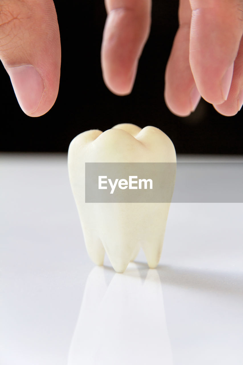 Cropped hand holding dentures on table against black background