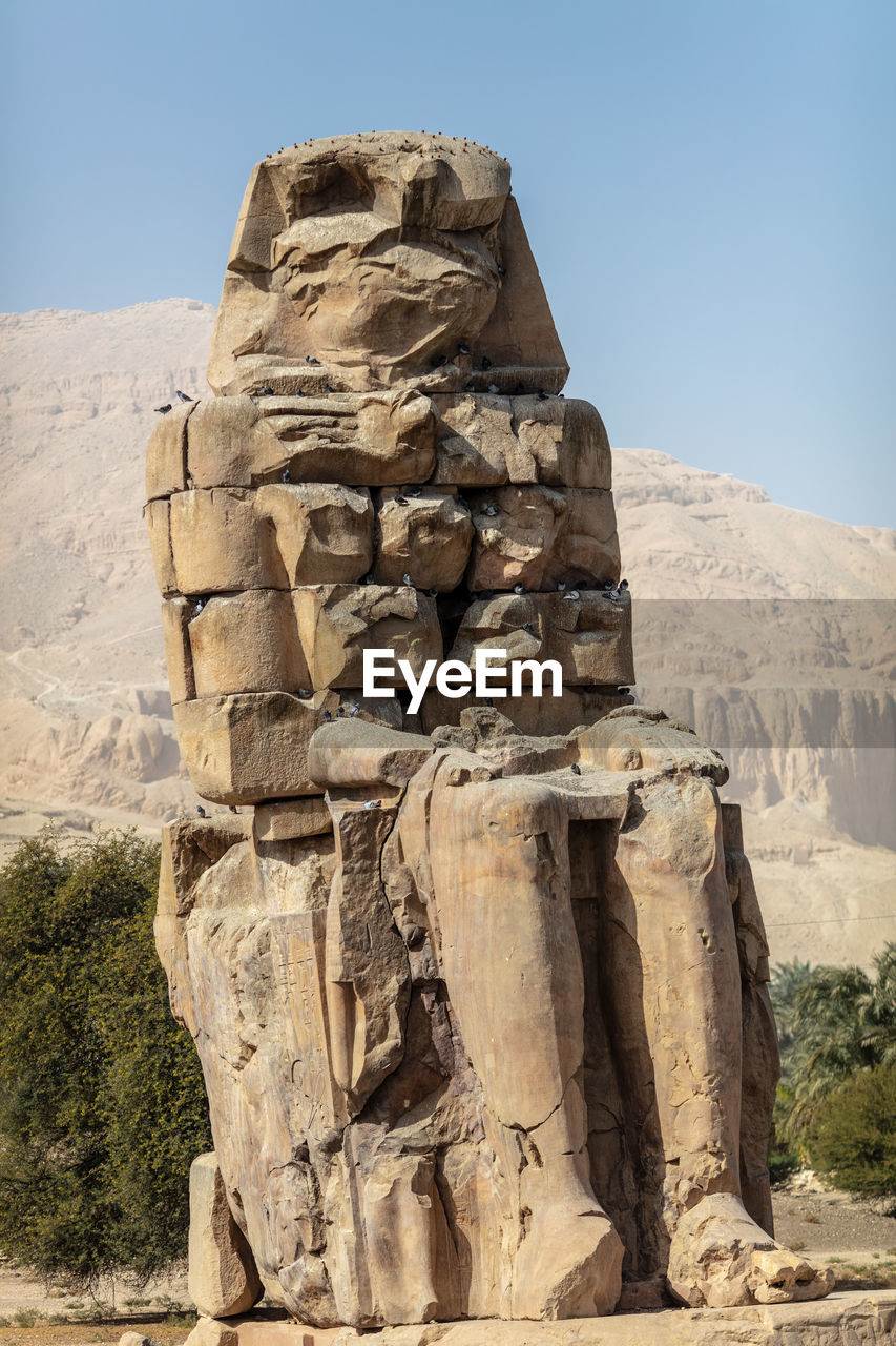 Beautiful daytime view of the colossi of memnon. two large stone figures depicting a seated pharaoh.