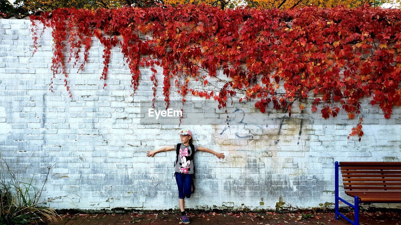 Portrait of smiling girl standing against wall during autumn