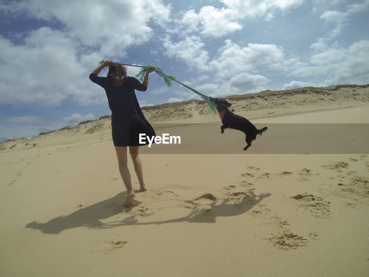 Rear view full length of woman playing with dog at sandy beach against sky